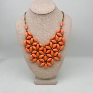 May include: A coral coloured statement necklace with a floral design. The necklace is made of plastic beads and gold chain.