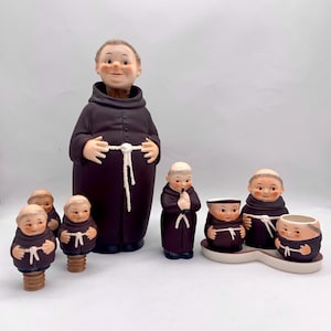 Puede incluir: Conjunto de figuras de monjes de cerámica, que incluye un gran tapón de botella de monje y tapones de botella de monje más pequeños. Los monjes llevan túnicas marrones y cinturones de cuerda blanca.