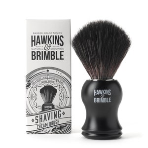 Op de afbeelding: Zwarte scheerschuimborstel met natuurlijke haren en een zwarte handgreep. De borstel is verpakt in een doos met de merknaam "Hawkins & Brimble" en de tekst "Barber Grade Tonics".