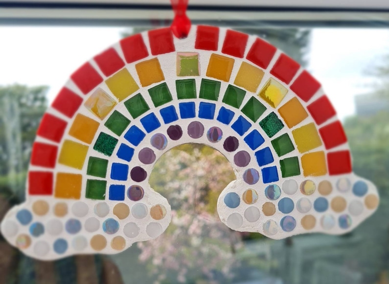 May include: A rainbow mosaic art piece with red, orange, yellow, green, blue, purple, and white tiles. The rainbow is shaped like an arch with clouds on either side. The clouds are also made of mosaic tiles.