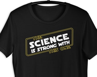 Op de afbeelding: Zwart T-shirt met een gele afbeelding met de tekst "The Science is Strong With This One" in een lettertype geïnspireerd door Star Wars.