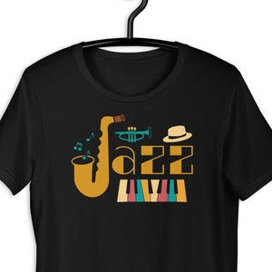 May include: Black t-shirt with a colourful graphic design featuring a saxophone, trumpet, hat, musical notes, and a keyboard. The word "Jazz" is written in a stylised font.