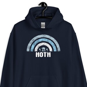 Könnte beinhalten: Marineblauer Kapuzenpullover mit einem verblassten Grafikdesign. Das Design zeigt einen Regenbogen mit hellblauen und weißen Streifen, AT-AT-Läufern und dem Wort "HOTH". Der Pullover hat eine Vordertasche und eine Kapuze mit Kordelzug.