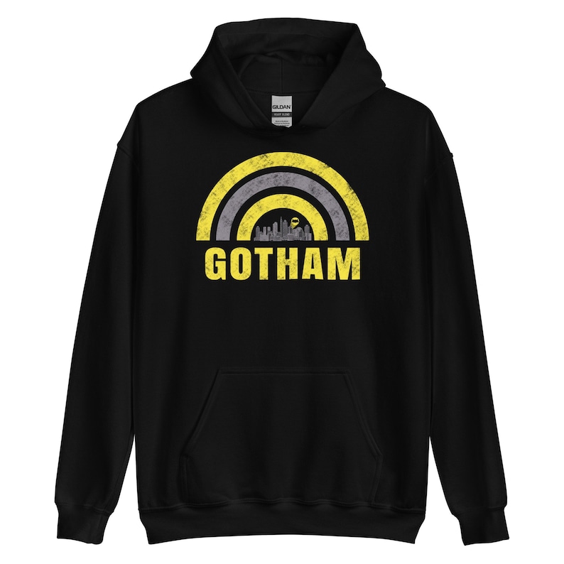 Puede incluir: Sudadera con capucha negra con un gr&aacute;fico desgastado amarillo y gris de una ciudad con la palabra "GOTHAM" debajo.