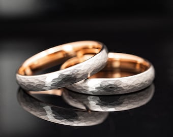 May include: Two rings featuring a textured, hammered silver-toned exterior and a smooth, polished rose gold-toned interior. The bands are positioned to overlap, showcasing the contrast between the metallic outer surface and the warm inner lining.