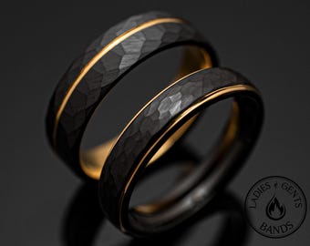 May include: Two rings with a dark, hammered, textured exterior surface and a smooth, gold-colored interior band. A thin, horizontal gold-colored line runs through the center of the outer surface. A circular logo with the text LADIES GENTS BANDS is visible.