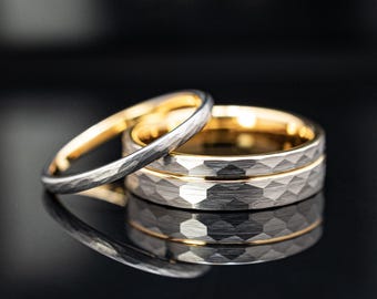 May include: Two rings with a hammered silver-toned exterior and a smooth gold-toned interior. The wider ring features a faceted, textured surface, while the thinner ring has a similar hammered finish. Both bands are metallic and reflective.