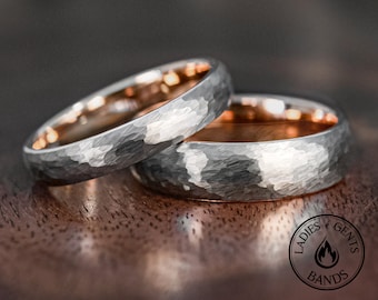 Può includere: Due anelli con un esterno argentato martellato e un interno liscio color oro rosa. Gli anelli presentano una superficie testurizzata e un logo circolare nell'angolo con il testo LADIES GENTS BANDS e un'icona a forma di fiamma.