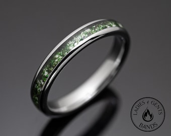 May include: A polished silver-toned metal ring featuring a central inlay of green moss-like material. The ring is displayed alongside a circular logo containing the text LADIES GENTS BANDS and a flame icon. The band has a smooth, reflective finish.