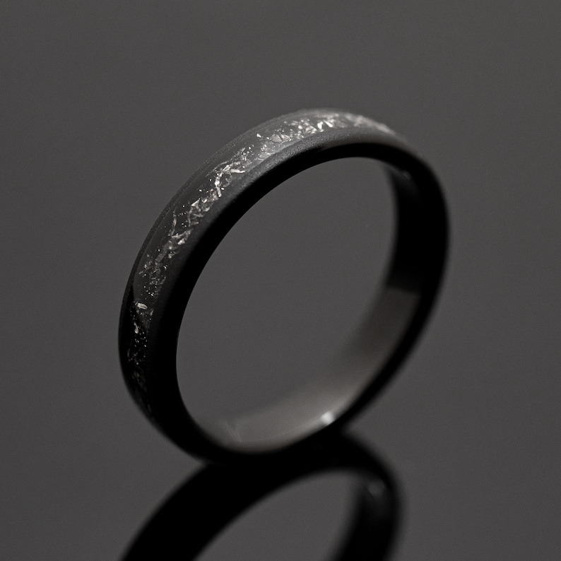 Peut inclure: Une bague noire avec une bande d'&eacute;clats argent&eacute;s. La bague est faite d'un mat&eacute;riau sombre et a une finition lisse et polie. La bague est de conception simple et &eacute;l&eacute;gante.