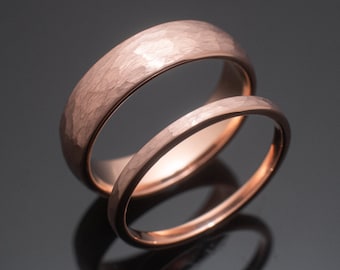 Puede incluir: Dos anillos de oro rosa con un acabado martillado y texturizado en la superficie exterior. Los anillos están colocados uno detrás del otro, mostrando un interior pulido y una textura exterior distintivamente irregular y mate en un tono metálico cálido.