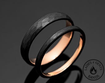 May include: Two black wedding bands with a hammered texture on the outside and a rose gold interior. The rings are displayed on a reflective surface, with a logo in the bottom right corner that reads "Ladies & Gents Bands."
