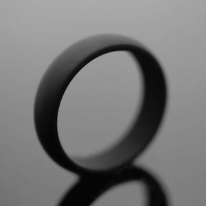 Op de afbeelding: Een effen zwarte ring met een gladde, matte afwerking en een afgerond buitenprofiel. De band heeft een eenvoudig, doorlopend cirkelvormig ontwerp zonder zichtbare gravures, stenen of extra decoratieve elementen op het oppervlak.