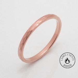 May include: A rose gold ring with a textured, hammered finish. The ring is thin and has a simple band design. The ring is displayed on a white background. The ring is a piece of jewelry.