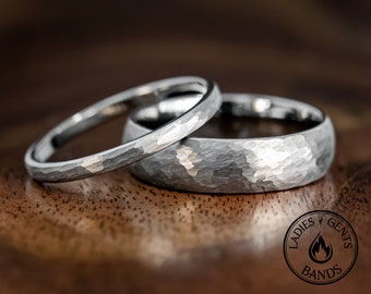 May include: Two silver-toned metal rings with a hammered, textured finish. The rings feature a rounded profile and a reflective surface. A circular logo in the bottom right corner contains the text LADIES & GENTS BANDS with a flame icon.