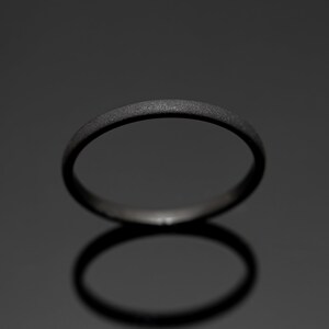 May include: A dark gray ring with a textured surface. The ring is circular and appears to be made of metal. The ring is set against a dark gray background, with its shadow visible below.
