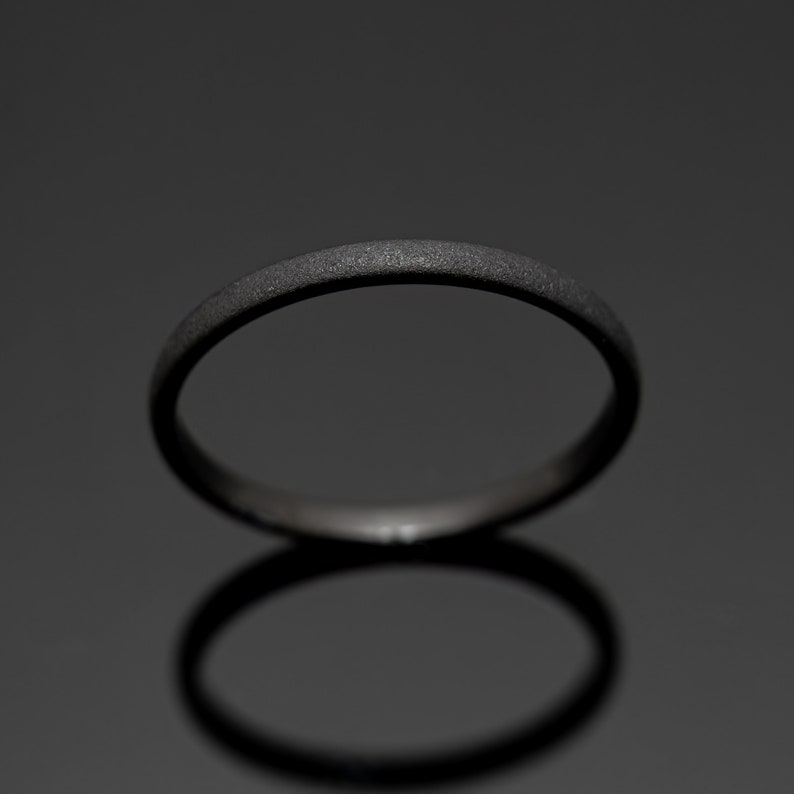 May include: A dark gray ring with a textured surface. The ring is circular and appears to be made of metal. The ring is set against a dark gray background, with its shadow visible below.