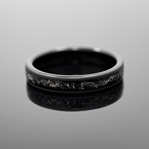 Peut inclure: Une bague noire avec une bande de mat&eacute;riau gris fonc&eacute; textur&eacute;. La bague est pos&eacute;e sur une surface r&eacute;fl&eacute;chissante, soulignant sa finition polie. Le design de la bague est simple, mais &eacute;l&eacute;gant, adapt&eacute; au port quotidien.