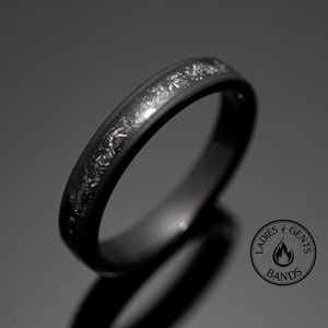 Peut inclure: Une bague noire avec une bande de paillettes argent&eacute;es. La bague est pos&eacute;e sur un fond sombre, l'accent &eacute;tant mis sur le design de la bague. Il s'agit d'un bijou, probablement pour un usage quotidien.