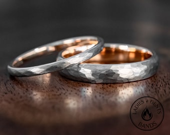 May include: Two rings with a hammered silver-toned exterior and a smooth rose gold-toned interior. The rings feature a textured surface and a circular logo in the corner with the text LADIES GENTS BANDS and a flame icon.