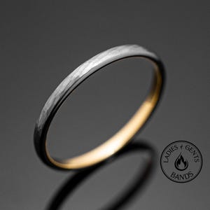 May include: A thin, hammered silver band with a gold inner edge. The band is a simple design with a subtle texture.