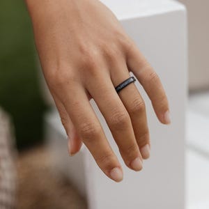 Peut inclure: Une bague noire &agrave; la surface textur&eacute;e est port&eacute;e au doigt. La bague semble &ecirc;tre faite d'un mat&eacute;riau sombre, peut-&ecirc;tre du m&eacute;tal ou un composite. La bague est de style simple.