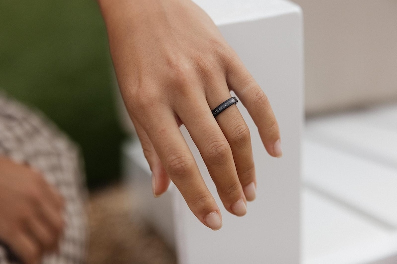 Peut inclure: Une bague noire &agrave; la surface textur&eacute;e est port&eacute;e au doigt. La bague semble &ecirc;tre faite d'un mat&eacute;riau sombre, peut-&ecirc;tre du m&eacute;tal ou un composite. La bague est de style simple.