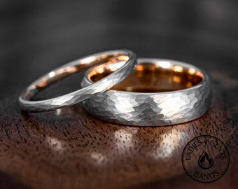 May include: Two rings with a hammered silver-toned exterior and a smooth rose gold-toned interior. The rings are positioned together, and a circular logo featuring the text LADIES GENTS BANDS with a flame icon is visible in the corner.