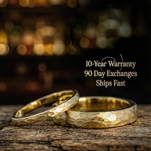 Puede incluir: Dos alianzas de boda doradas con una textura martillada se muestran sobre una superficie de madera. Los anillos están enfocados, con un fondo borroso. El texto "10-Year Warranty 90 Day Exchanges Ships Fast" también es visible.