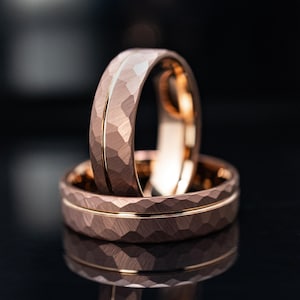 Pode incluir: Dois anéis de ouro rosa com acabamento martelado e texturizado. Cada banda apresenta um sulco horizontal fino, liso e polido no centro, criando um contraste entre a superfície fosca facetada e a linha brilhante e rebaixada.