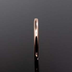 May include: A polished rose gold ring with a smooth, rounded band profile. The metal surface is highly reflective, showing a warm metallic hue and a seamless, continuous circular shape captured from a side-on perspective against a dark background.