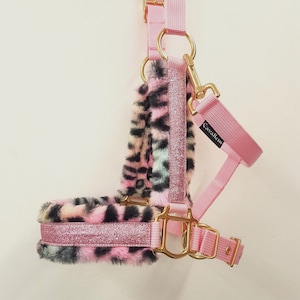 Pode incluir: Cabresto rosa para cavalos com ferragens douradas e um detalhe rosa brilhante. O cabresto apresenta um design de estampa de leopardo com pelo rosa, preto e cinza. A marca "Cavallini" é visível na correia.
