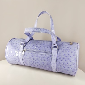 May include: A lavender-coloured, cylindrical duffel bag with a textured, ostrich-like pattern. The bag has a single top handle and a zipper closure.