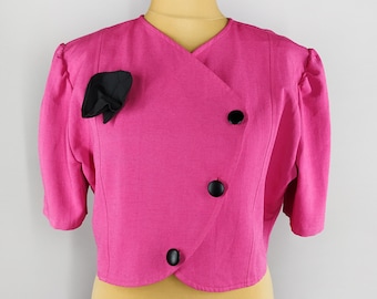 May include: A pink cropped jacket with a black bow and black buttons. The jacket has a diagonal closure and short sleeves.
