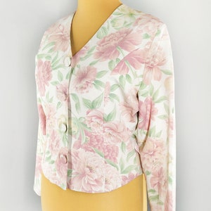 May include: A white floral print blazer with pink flowers and green leaves. The blazer has a v-neck and long sleeves.