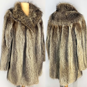 May include: A vintage fur coat in shades of brown and tan, displayed on a mannequin. The coat features a wide collar and a long, flowing design. The fur appears soft and luxurious, with a natural, textured appearance.