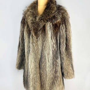 May include: A vintage fur coat with a wide collar and long sleeves. The coat is displayed on a mannequin, showcasing its brown and gray tones. The fur appears soft and luxurious, with a natural, textured appearance.