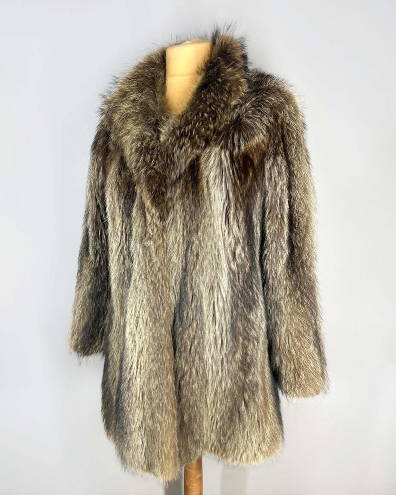 May include: A vintage fur coat with a wide collar and long sleeves. The coat is displayed on a mannequin, showcasing its brown and gray tones. The fur appears soft and luxurious, with a natural, textured appearance.