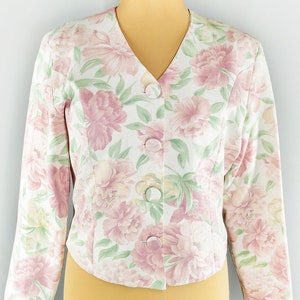 May include: A white floral print cropped jacket with a v-neck and button closure. The jacket has a pink and green floral pattern.