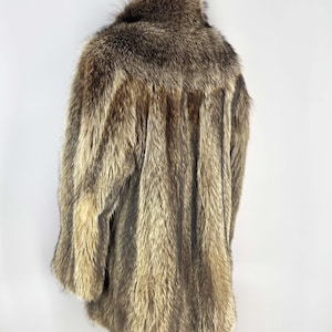 May include: A vintage fur coat with a natural color palette of browns and tans. The coat has a wide collar and a long, flowing design. The fur appears to be in good condition, with a soft and textured appearance. The coat is displayed on a wooden stand.