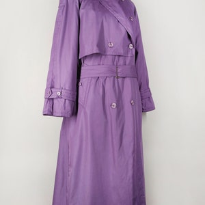 May include: A long, purple trench coat with a double-breasted closure, a belt, and a collar. The coat has a classic design and is made of a smooth, lightweight fabric.
