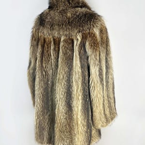 May include: A vintage fur coat in shades of brown and tan, with a textured, striped pattern. The coat has a collar and long sleeves, and appears to be in good condition. The coat is displayed on a wooden hanger against a white background.