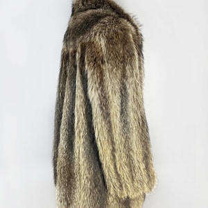 May include: A long, faux fur coat in shades of brown and tan. The coat has a collar and long sleeves. The fur appears soft and plush, with a natural-looking texture. The coat is displayed on a wooden hanger.