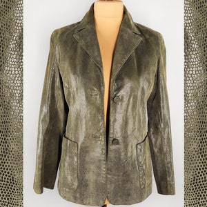 Może przedstawiać: Zielony skórzany blazer z fakturowanym wzorem skóry węża. Blazer ma pojedyncze zapięcie na guzik i dwie kieszenie.