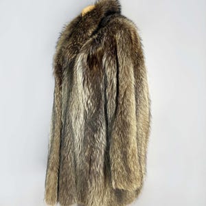 May include: A full-length fur coat in shades of brown, gray, and tan. The coat has a wide collar and long sleeves. The fur appears thick and luxurious, with a natural, textured appearance. The coat is displayed on a wooden hanger.