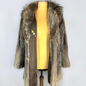 May include: A vintage fur coat with a brown and gray pattern. The coat has a wide collar and is open, revealing a brown lining. The coat is displayed on a yellow mannequin.