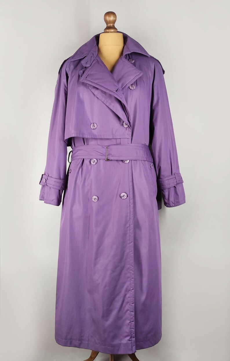 May include: A long, purple trench coat with a double-breasted closure, a belt, and a collar.