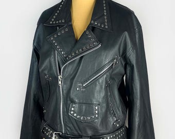 May include: Black leather jacket with silver-tone studs on the collar, lapels, pockets, and belt. The jacket features a zipper closure, multiple zippered pockets, and a studded belt. The jacket is displayed on a mannequin.