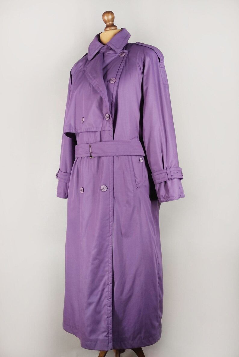 May include: A long, purple trench coat with a double-breasted closure, a belt, and a collar.