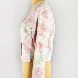 May include: A white cropped jacket with a pink and green floral print. The jacket has long sleeves and a button-up front.